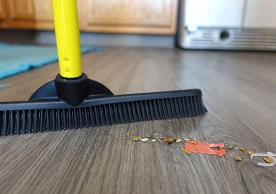 Close up on pile of crumbs, rubbish and dog hair being swept up by rubber-bristled broom.