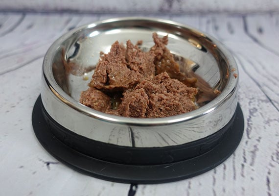 Canned wet dog food sitting in stainless steel flat-faced dog bowl.